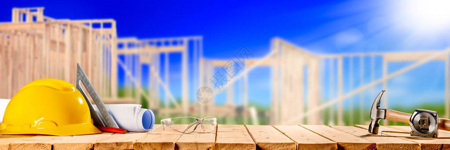 在木桌上的建筑工具与背景中的新房子框架图片