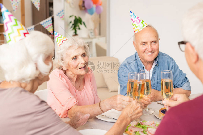 一群快乐的资深朋友在餐桌前与香槟笛图片