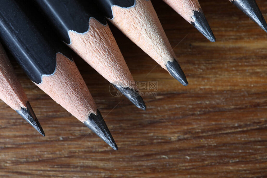 在木桌上排成一排的几支黑色铅笔的顶视图图片