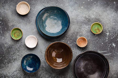 质朴的灰色混凝土背景上的各种陶瓷手工制作的彩色空盘子和碗图片