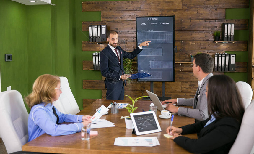 穿着西装的商人在与他的同事开会时指着电视屏幕上的图表在会议室图片