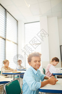 坐在学校书桌边看着摄影机微笑复制空间的滑头发毛的喜悦混合种族男图片