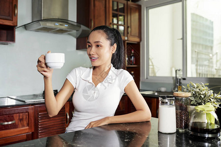 衣着便衣的亚洲青年妇女坐在厨房的桌子上图片