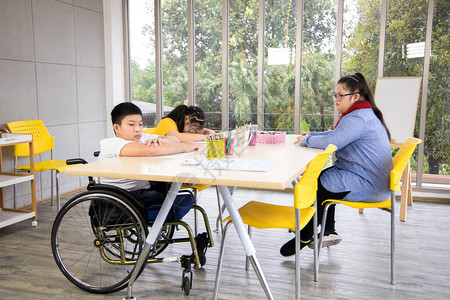 蒙氏教室两个患有唐氏综合症的女孩和坐在轮椅上的残疾男孩坐在教室里背景