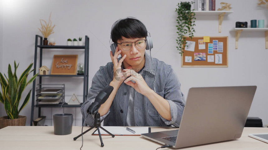 亚洲青年商人使用麦克风和笔记本电脑在家庭工作室播客和录制在线脱口秀节目图片