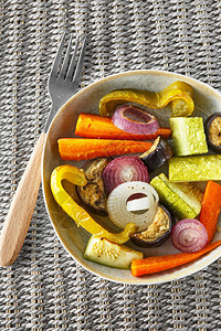 烤蔬菜在盘子上与柳条服务垫上的餐具混合图片