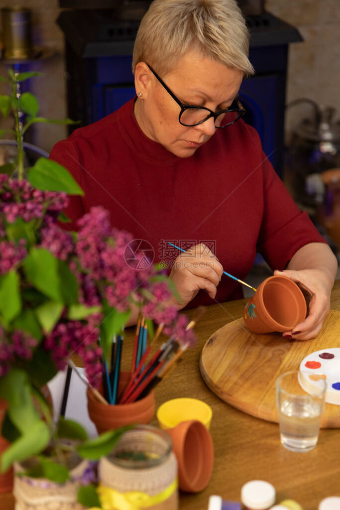 美丽的成年女艺术家在艺术家庭工作室的陶罐上画丁香花手工锅DIY创意陶艺工作坊装饰画具生活方图片