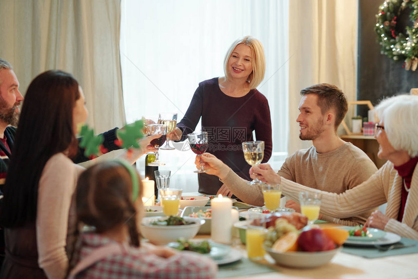 金发成年女及其家庭成员在家节日晚宴期间与酒杯和餐桌上餐桌相缠的美图片