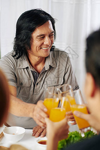 微笑的中年男子在晚餐时与家人一起举杯果汁图片