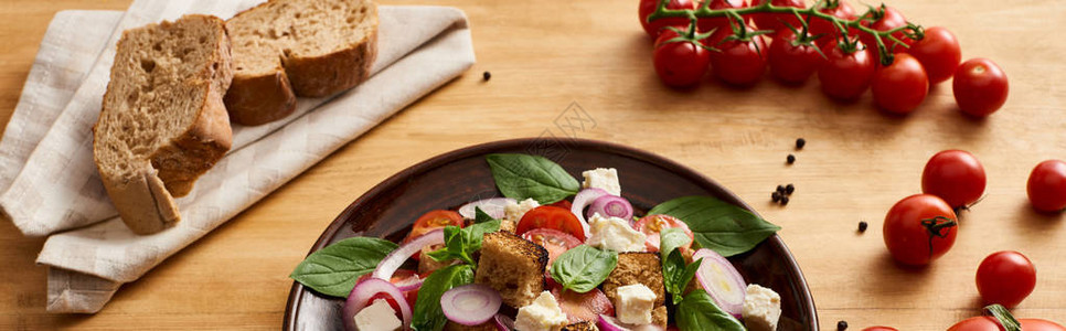 意大利美味的蔬菜沙拉潘扎尼拉在西红柿和面包附近的木制餐桌上用盘子做图片