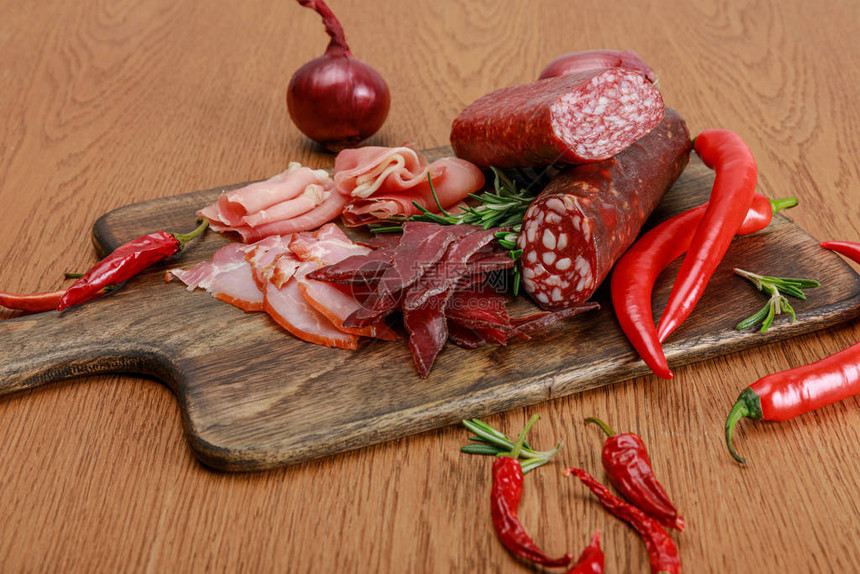 木桌上的美味肉拼盘配以辣椒和迷迭香图片