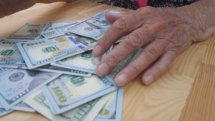 祖母怀里从桌子上扫出一捆散落的百元钞票皱巴的女手从桌子上拿出一堆的外币顶图片