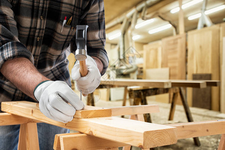 特写木匠用他的双手用锤子和钉子的手套保护着一块木板建筑图片