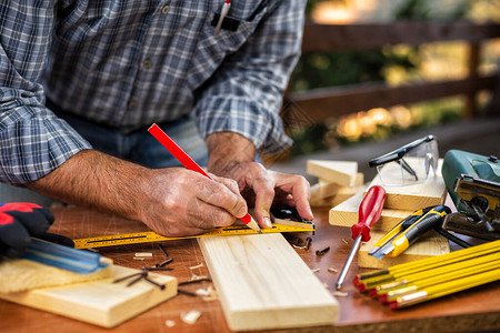 成年木匠工用铅笔和木匠的方格在木桌上追踪切割线图片