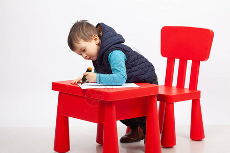 白人背景的可爱小男孩绘画红色桌椅和子图片