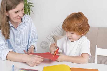 带着保姆母亲或老师的红发小男孩坐在房间的桌子旁图片