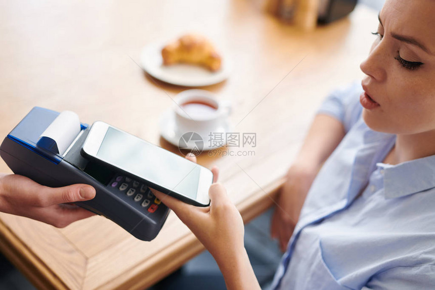 收紧坐在桌边并支付餐饮用智能手机早餐费用的严重年轻妇图片