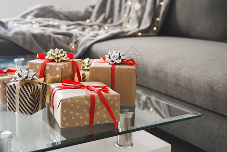 客厅玻璃咖啡桌上用工艺纸包裹的礼品盒带毯子的沙发床和装饰灯作为背图片