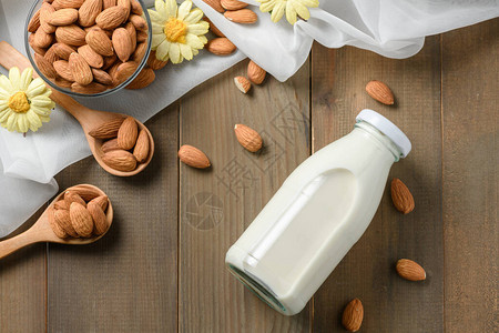 鲜奶和杏仁坚果的瓶装在木桌背景上图片