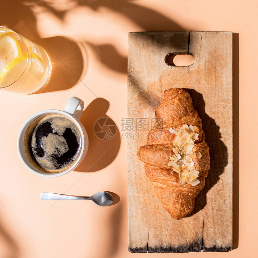 在米色桌子上享用早餐的木制切菜板上的咖啡水和羊角图片