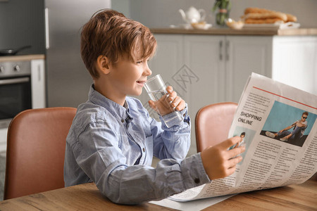 阅读报纸和厨房饮用水的可爱小男孩在厨房图片