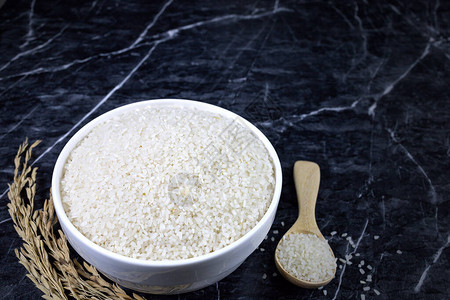 碎米泰国茉莉花大米在白陶瓷碗和黑大理石桌上的木背景