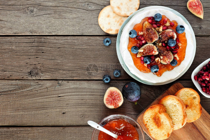 用无花果和酱蓝莓石榴和坚果装饰的烤布里干酪开胃菜俯视图侧边框与质朴的木质背图片
