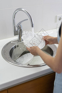 垂直照片妇女手持餐具用水泼池洗盘子站在白色明亮厨房的纵向照片切图片