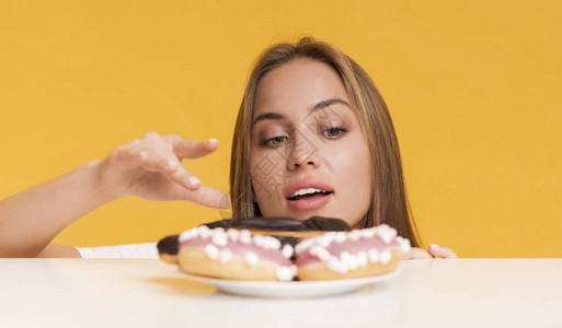 饥饿的年轻女从花牌上吃甜食图片