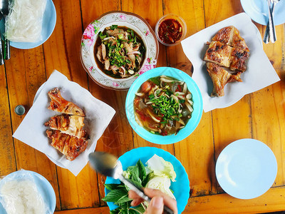 当地带手和许多板块的泰国食物鸡肉粘糊大米沙拉辣汤猪肠和蔬菜的图片
