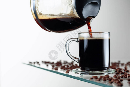 玻璃桌上的玻璃杯中的黑咖啡咖啡从咖啡机倒进杯子图片