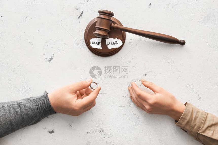 夫妻手握结婚戒指和法官在白种背景上的锤子图片