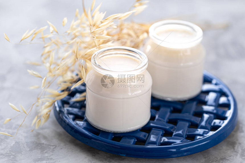 非乳制品替代品蔬菜牛奶或酸奶在白色背景上的一个罐子里蓝色支架上的玻璃罐中的燕麦奶油和燕麦小枝健康饮食概念图片