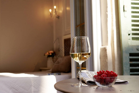 花瓶中的花束一杯白葡萄酒和一盘新鲜的草莓和红卷盆子在房图片