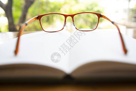 木制桌上有白笔记本的橙色眼镜Bookeh花园背景关闭和宏观镜头选择焦图片