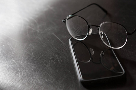 选择地聚焦眼镜对黑色背景的智能手机和以光和阴影复图片