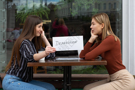 持有白纸的妇女手头贴着萧条一词的标签两名妇女在街头咖啡馆发言隐图片