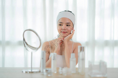 美丽的亚洲年轻女子的肖像照着她的皮肤坐在卧室的镜子旁图片
