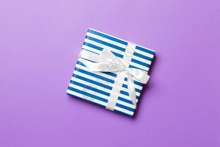 用紫色背景上的白丝带用纸包裹圣诞节或其他节日手工制作的礼物图片