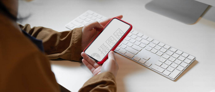 白色办公桌键盘上手握空白屏幕智能手机的图片