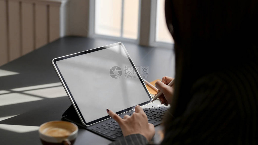 在舒适工作场所的黑桌子上用塑料和咖啡杯制成的数码平板电脑工作的女图片