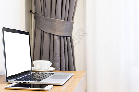 带智能手机的空白屏幕笔记本电脑和客房酒店背景木桌内部砖墙上的咖啡杯图片