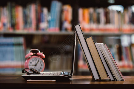 书架背景模糊的图书馆室工作场所的笔记本电脑和书籍粉色钟表教育学图片