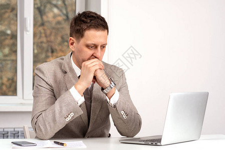 穿着米色西装坐在笔记本电脑上工作的严肃年轻人的半身肖像图片