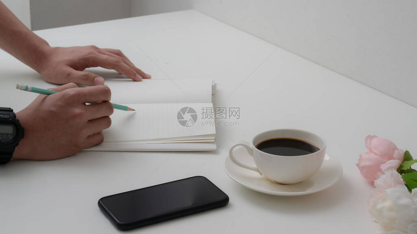 男大学生的裁剪镜头在笔记本上用咖啡杯和白桌上智能手图片