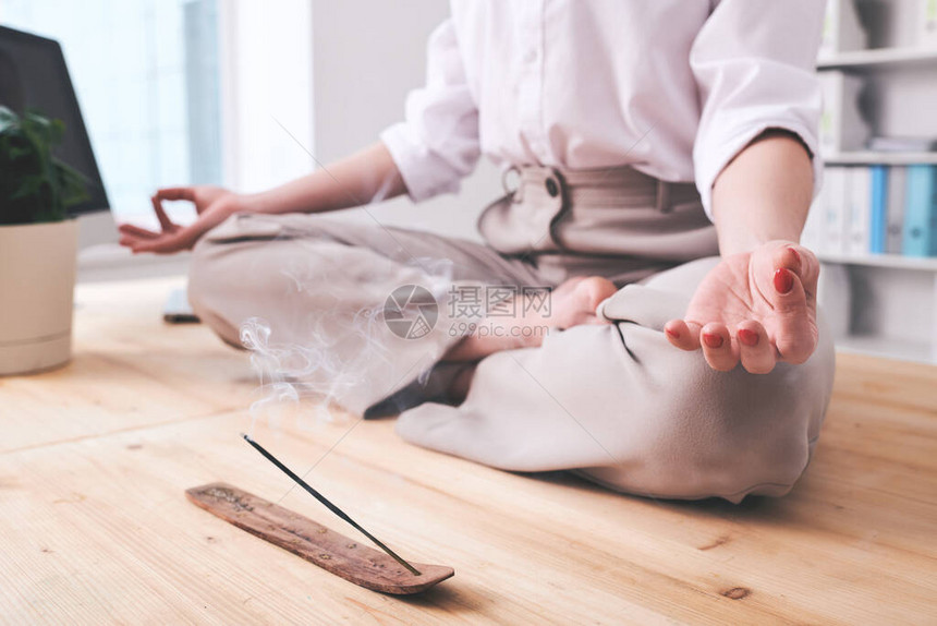 身穿正装坐在办公桌边的年轻商业女商人用烟雾棍子在附近抽着香味棍子图片