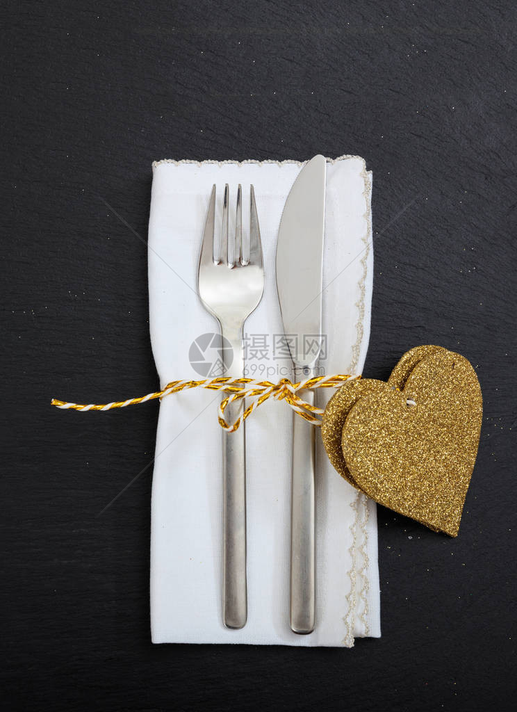 刀叉餐具白色餐巾纸和黑色背景上的金色心形图片