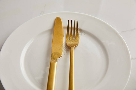 大理石桌子上干净的白盘子上的金刀和叉子图片