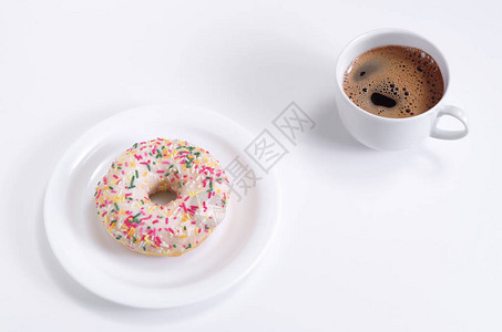 在白桌上的盘子上和咖啡杯上撒着冰甜圈图片