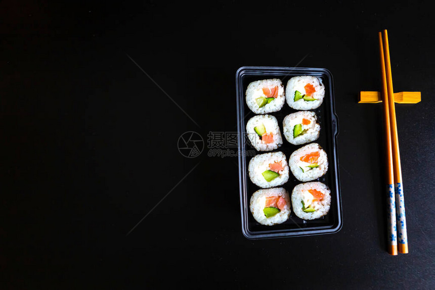 黑桌上的盒子里有一套寿司卷和筷子平面顶视图片